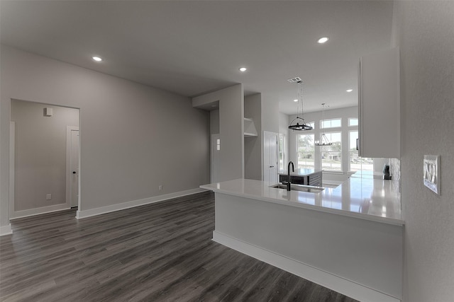 kitchen with dark wood finished floors, a peninsula, recessed lighting, a sink, and light countertops