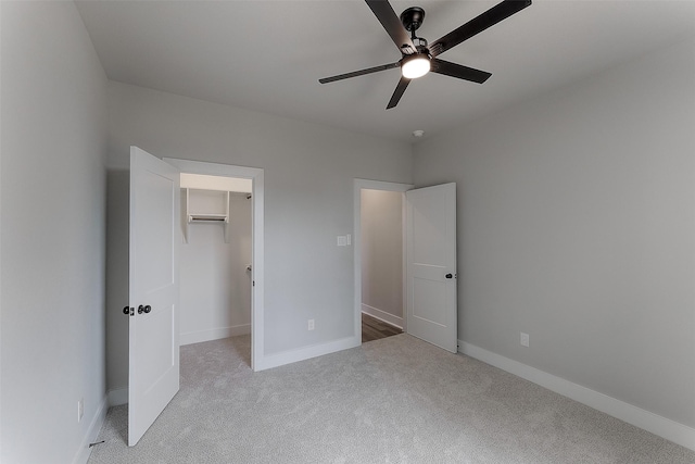 unfurnished bedroom featuring a walk in closet, ceiling fan, baseboards, and light carpet