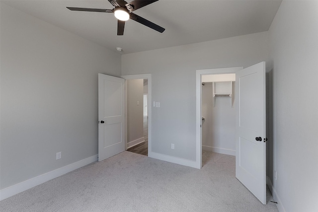 unfurnished bedroom featuring a walk in closet, carpet floors, baseboards, and a ceiling fan