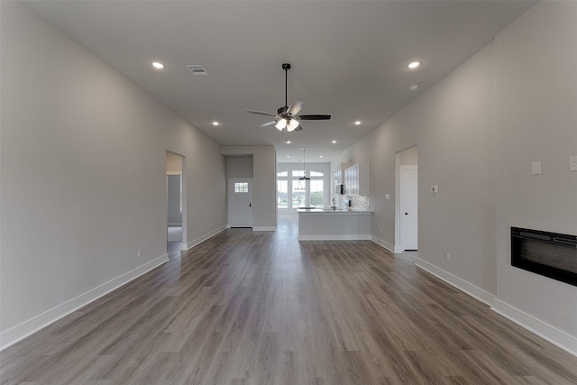 unfurnished living room with baseboards, ceiling fan, recessed lighting, wood finished floors, and a glass covered fireplace