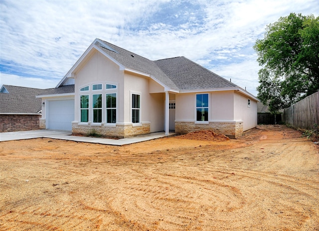 view of front facade featuring fence, stone siding, roof with shingles, and stucco siding