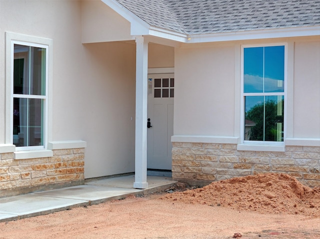 entrance to property with stone siding, roof with shingles, and stucco siding