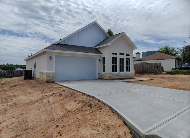 view of front of property featuring central air condition unit, driveway, stone siding, fence, and a garage