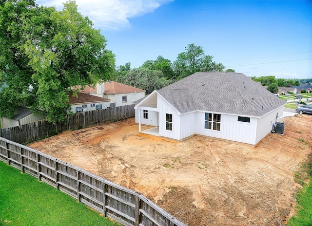 rear view of property with central AC unit, a fenced backyard, and roof with shingles