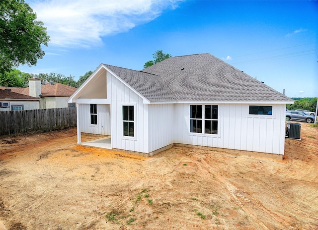 rear view of house with cooling unit, fence, roof with shingles, a patio area, and board and batten siding