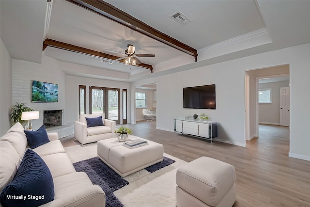 living room featuring light hardwood / wood-style flooring, a large fireplace, ornamental molding, a tray ceiling, and beamed ceiling