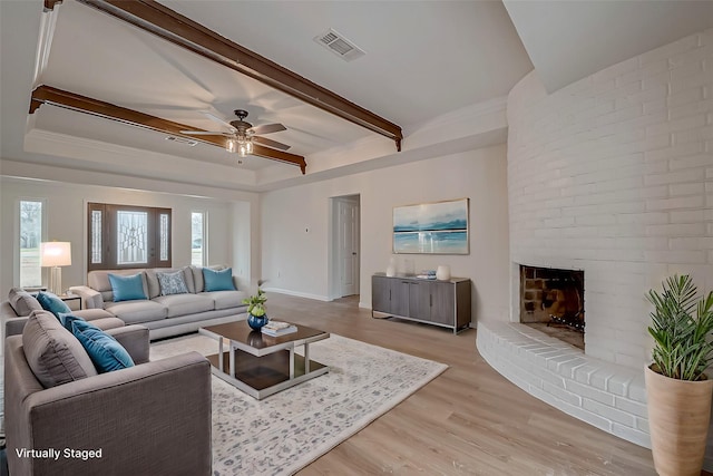 living room featuring ceiling fan, a fireplace, light hardwood / wood-style floors, a raised ceiling, and beamed ceiling