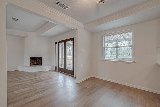 unfurnished living room with french doors, a brick fireplace, light hardwood / wood-style flooring, a textured ceiling, and ornamental molding