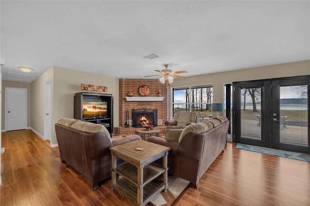 living room featuring ceiling fan, a textured ceiling, a brick fireplace, and light wood-type flooring