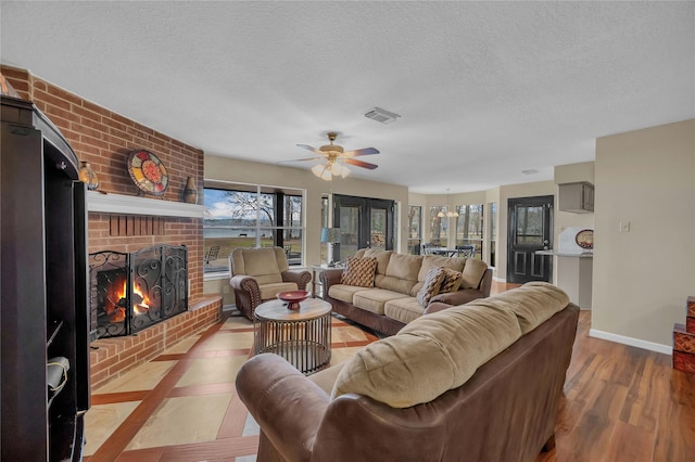 living room with a brick fireplace, light hardwood / wood-style flooring, a textured ceiling, and ceiling fan