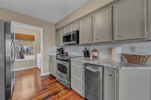 kitchen featuring light wood-type flooring, gray cabinets, stainless steel appliances, light stone countertops, and backsplash