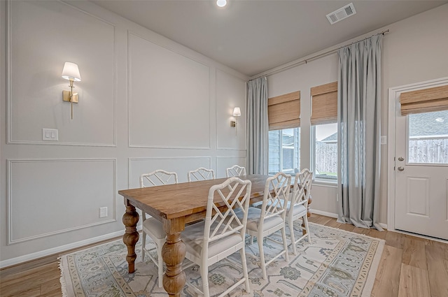 dining area featuring visible vents, baseboards, a decorative wall, and light wood-type flooring