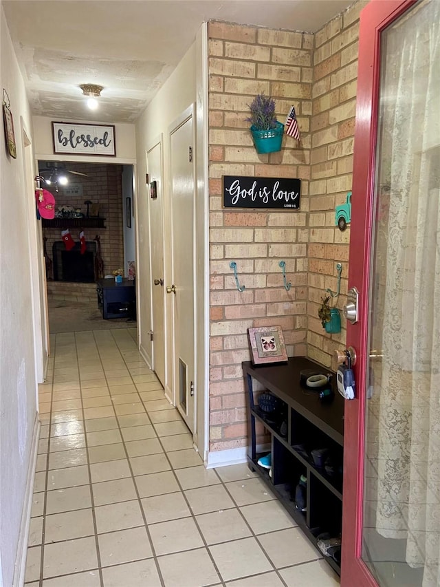 hall featuring light tile patterned floors and brick wall