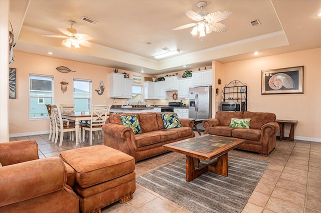 tiled living room with ceiling fan, sink, crown molding, and a raised ceiling