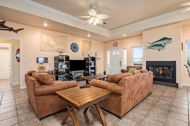 tiled living room featuring ceiling fan, ornamental molding, a large fireplace, and a raised ceiling