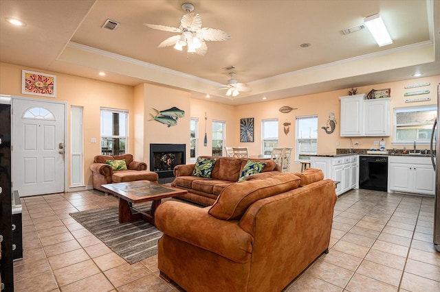 tiled living room with ceiling fan, sink, crown molding, and a raised ceiling