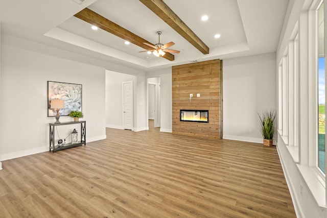 unfurnished living room featuring a tray ceiling, a fireplace, light hardwood / wood-style floors, and ceiling fan