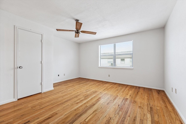 empty room featuring a textured ceiling, a ceiling fan, light wood-style flooring, and baseboards