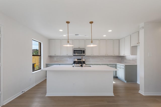 kitchen with an island with sink, white cabinetry, sink, hanging light fixtures, and stainless steel appliances