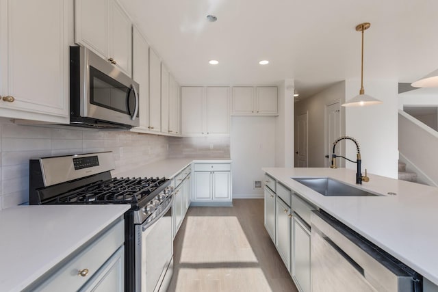 kitchen with sink, appliances with stainless steel finishes, white cabinetry, tasteful backsplash, and decorative light fixtures