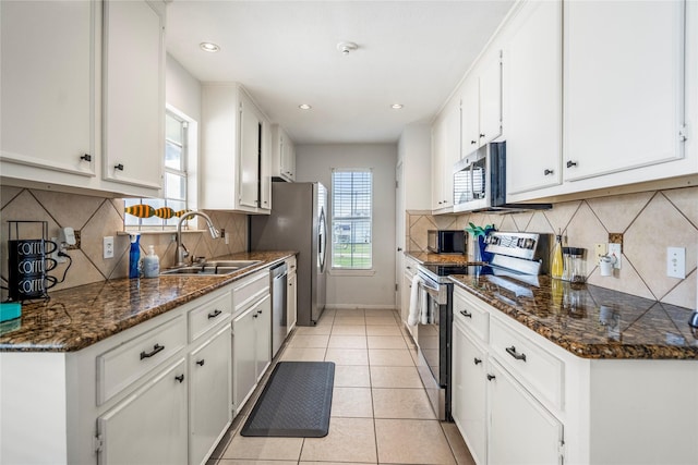 kitchen featuring sink, white cabinetry, dark stone countertops, light tile patterned floors, and stainless steel appliances