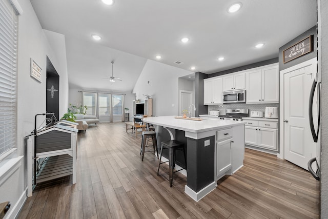 kitchen featuring appliances with stainless steel finishes, a breakfast bar area, white cabinets, a center island with sink, and light hardwood / wood-style flooring