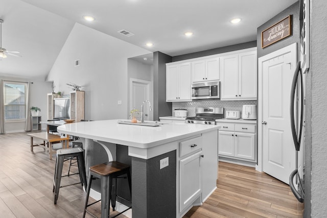 kitchen with appliances with stainless steel finishes, a kitchen breakfast bar, an island with sink, and white cabinets