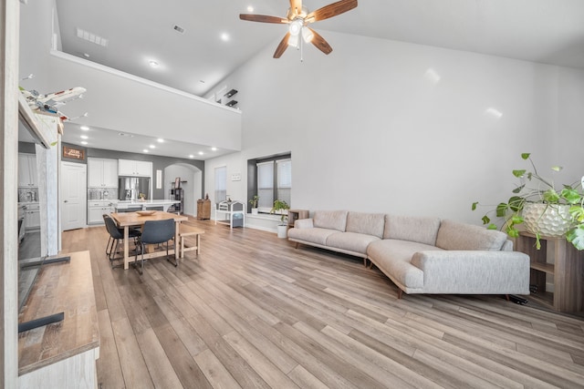 living room featuring ceiling fan, light hardwood / wood-style floors, and a high ceiling