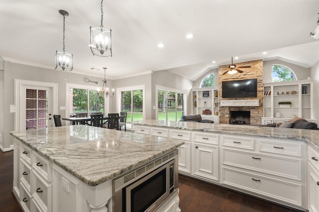 kitchen with stainless steel microwave, hanging light fixtures, white cabinets, and a kitchen island