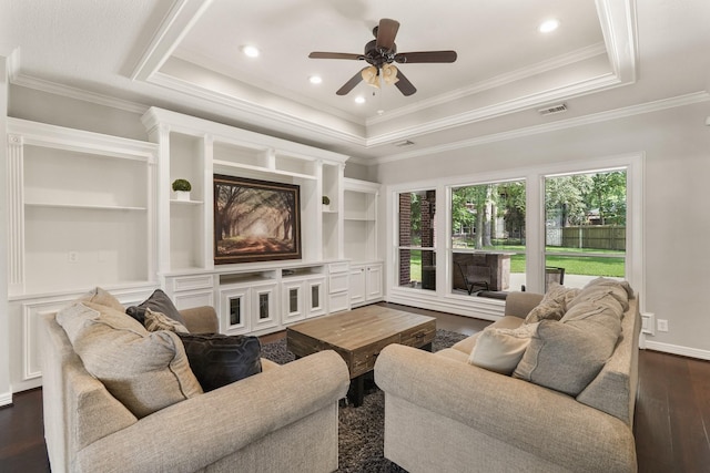 living room featuring crown molding, a tray ceiling, dark hardwood / wood-style flooring, and built in features