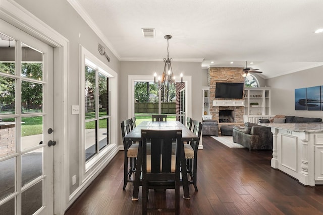 dining space featuring dark wood-type flooring, ornamental molding, a stone fireplace, and a wealth of natural light