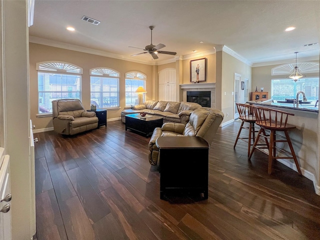 living room with a tiled fireplace, crown molding, a healthy amount of sunlight, and dark hardwood / wood-style flooring