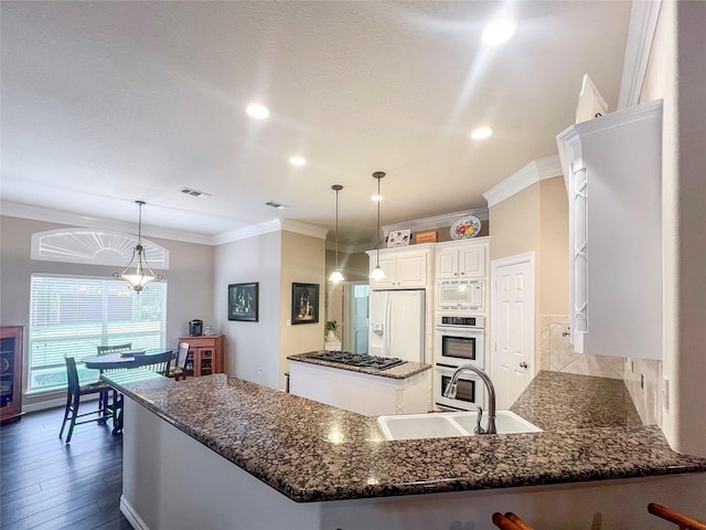 kitchen featuring appliances with stainless steel finishes, sink, white cabinets, dark stone counters, and hanging light fixtures