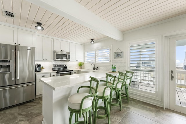 kitchen with white cabinetry, appliances with stainless steel finishes, a kitchen bar, and backsplash