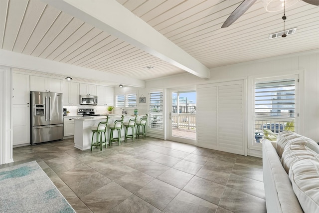 kitchen featuring beamed ceiling, white cabinetry, a breakfast bar area, hanging light fixtures, and stainless steel appliances