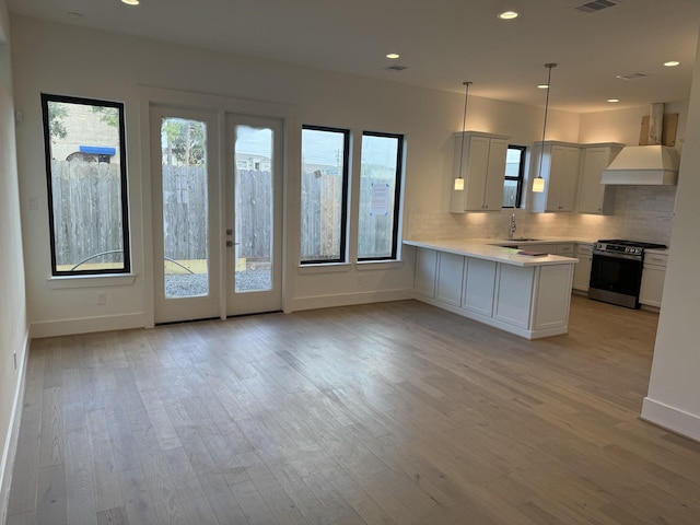 kitchen with white cabinets, hanging light fixtures, kitchen peninsula, custom range hood, and stainless steel range oven