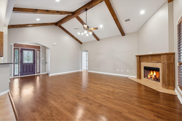 unfurnished living room featuring high vaulted ceiling, a fireplace, beamed ceiling, hardwood / wood-style flooring, and ceiling fan