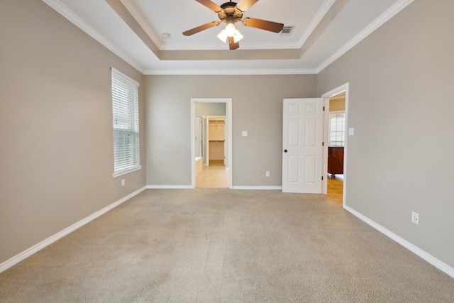 unfurnished bedroom featuring ornamental molding, a spacious closet, ceiling fan, a tray ceiling, and light carpet