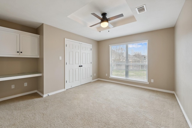 unfurnished bedroom with ceiling fan, a closet, built in desk, and light carpet