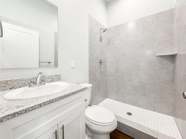 bathroom featuring vanity, toilet, wood-type flooring, and a tile shower