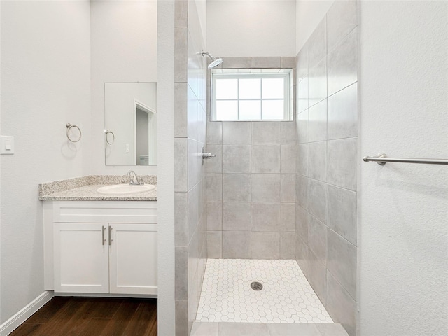 bathroom with wood-type flooring, tiled shower, and vanity