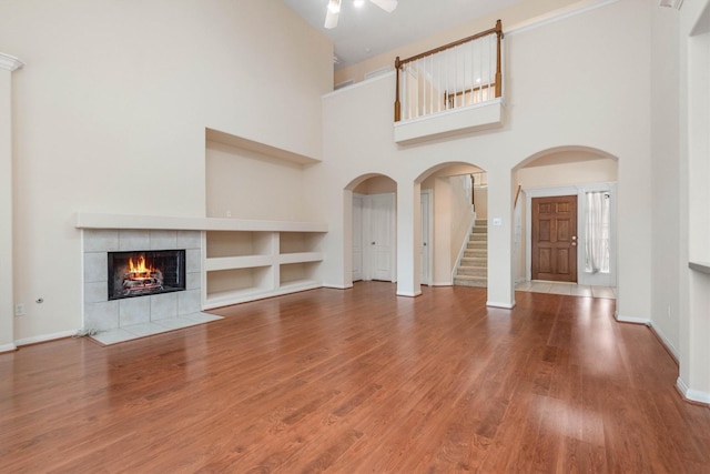 unfurnished living room with a tiled fireplace, wood-type flooring, a high ceiling, and built in shelves