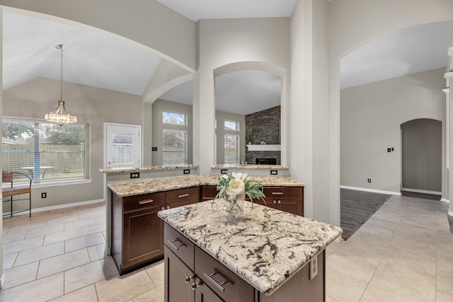 kitchen with a kitchen island, decorative light fixtures, lofted ceiling, light stone countertops, and dark brown cabinets