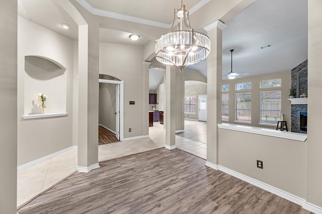 unfurnished dining area with crown molding, wood-type flooring, a stone fireplace, and ceiling fan with notable chandelier