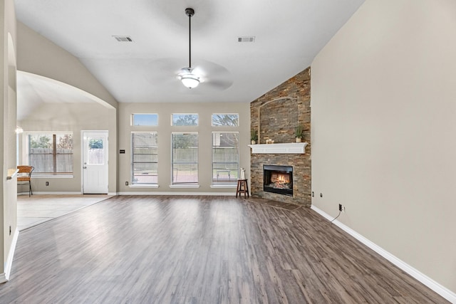 unfurnished living room with lofted ceiling, a stone fireplace, ceiling fan, and light hardwood / wood-style flooring