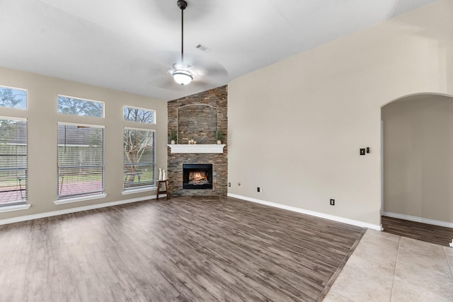 unfurnished living room featuring ceiling fan, a stone fireplace, vaulted ceiling, and light hardwood / wood-style flooring