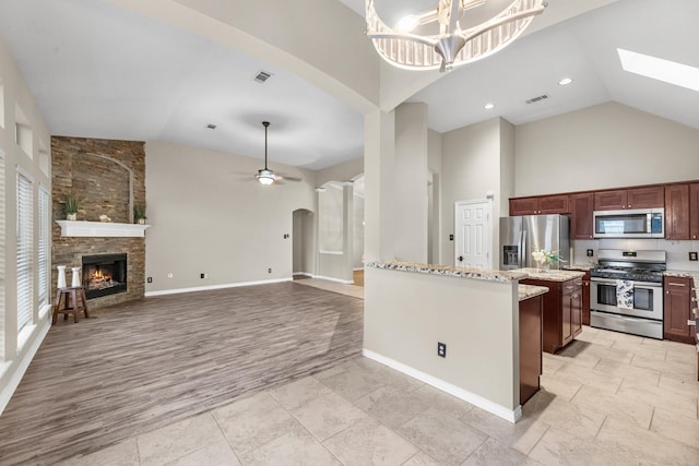 kitchen with a center island, high vaulted ceiling, hanging light fixtures, stainless steel appliances, and light stone countertops