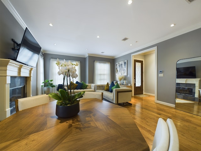 dining area featuring a tiled fireplace, crown molding, and light wood-type flooring