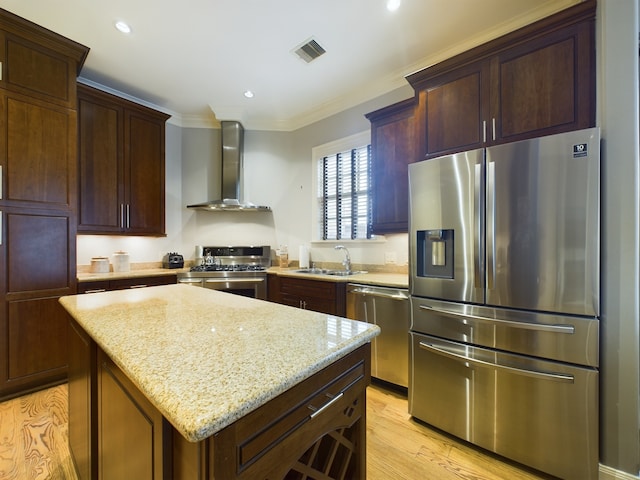 kitchen with wall chimney exhaust hood, sink, a kitchen island, stainless steel appliances, and light stone countertops