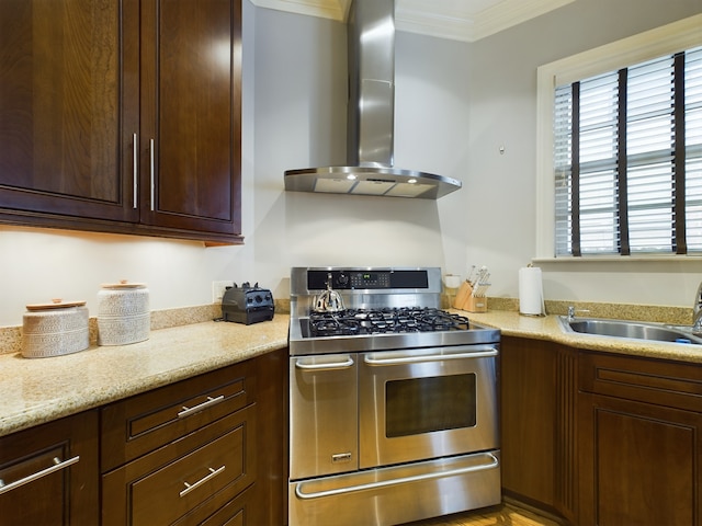 kitchen featuring wall chimney exhaust hood, sink, crown molding, light stone counters, and range with two ovens